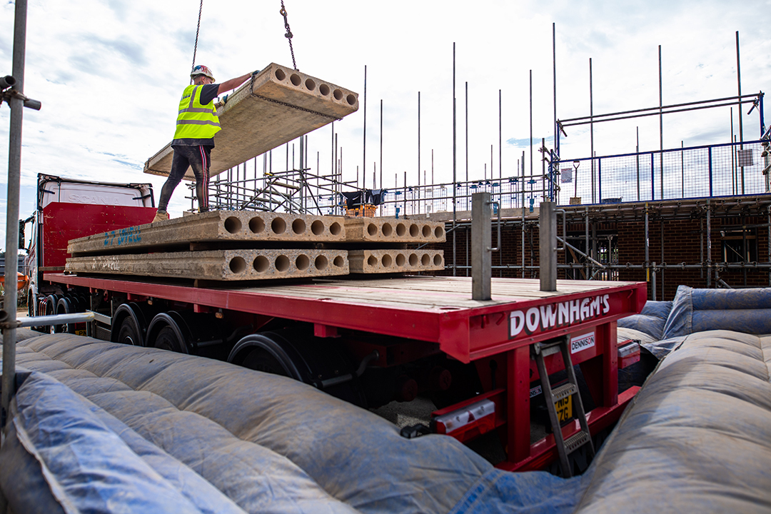 Red lorry with concrete planks being lifted off by worker in hi-vis and hardhat